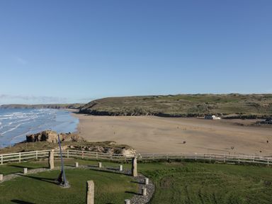 A beach with sand dunes and a circular stone and metal structure on grass at Chapel Rock View The Dunes in Perranporth