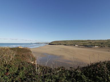 A sandy beach with ocean waves and dunes in the background at Chapel Rock View The Dunes Perranporth