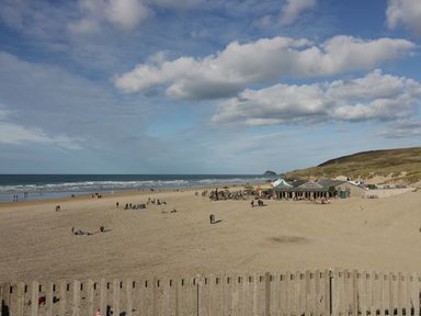 A sandy beach with people walking and a building near dunes at Chapel Rock View The Dunes in Perranporth
