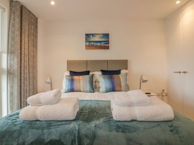 A bedroom with a bed with blue and brown pillows white towels and a beach painting at Chapel Rock View The Dunes in Perranporth