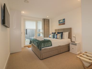 A bedroom with a double bed pillows bedside table and wall-mounted television at Chapel Rock View The Dunes in Perranporth