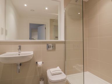 A bathroom with a wall-mounted sink toilet with towels and a glass shower enclosure at Chapel Rock View The Dunes in Perranporth