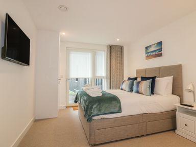 A bedroom with a bed with pillows and folded towels a bedside table with a lamp and a television on the wall at Chapel Rock View The Dunes in Perranporth