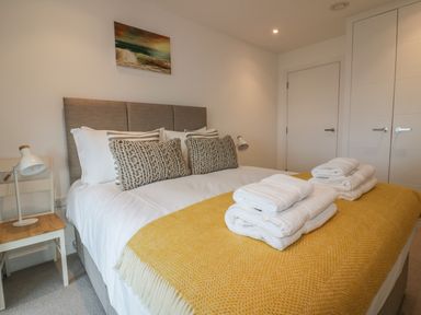 A bedroom with a bed covered in white sheets and yellow blanket with towels stacked on top at Chapel Rock View The Dunes in Perranporth