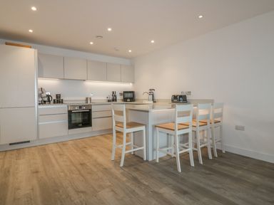 A kitchen with white cabinets an oven a microwave a toaster a coffee maker and four chairs at Chapel Rock View The Dunes in Perranporth