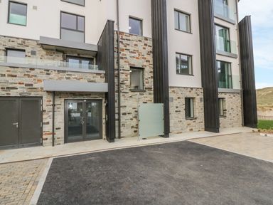 Exterior view of a modern building with stone and white walls and several windows at Chapel Rock View The Dunes in Perranporth