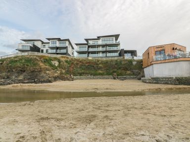 A sandy beach with a small body of water and modern buildings on a cliff at Chapel Rock View The Dunes in Perranporth