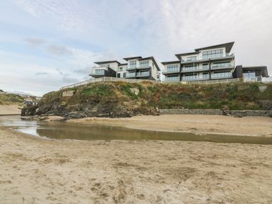 Modern apartment buildings on a cliff above a sandy beach with a small water pool at Chapel Rock View The Dunes in Perranporth