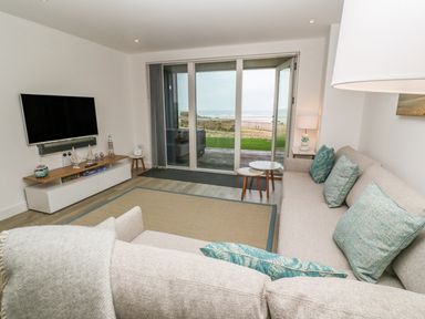 A living room with a sofa with cushions a television and a sliding glass door showing an outdoor view at Chapel Rock View The Dunes in Perranporth