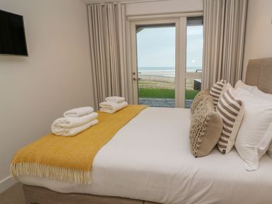 A bedroom with a bed with cushions and towels facing glass doors with a view of the garden and beach at Chapel Rock View The Dunes in Perranporth