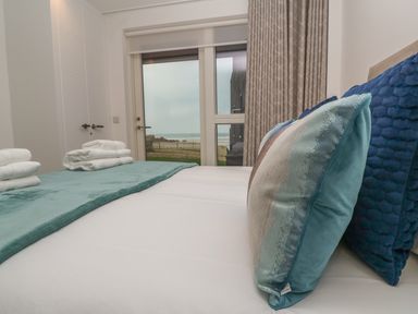 A bedroom with pillows and folded towels on a bed near a glass door showing an outdoor view at Chapel Rock View The Dunes in Perranporth