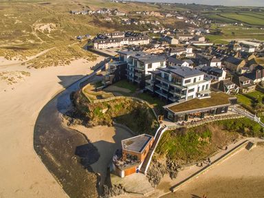 An aerial view of buildings by the beach with a sandy area and dunes at Chapel Rock View The Dunes in Perranporth