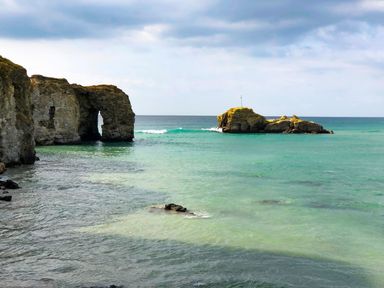 A coastal scene with a natural rock arch and a small rocky island in the sea at Chapel Rock View The Dunes in Perranporth