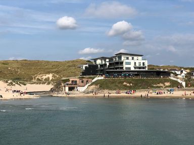 A beach with people and a modern building with a sign reading summerhouse on a hill at Chapel Rock View The Dunes in Perranporth