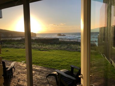A view of a lawn and ocean with chairs on a patio at Chapel Rock View The Dunes in Perranporth
