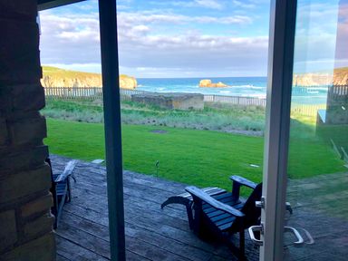 A wooden patio with two chairs overlooking a grassy area and ocean view at Chapel Rock View The Dunes in Perranporth