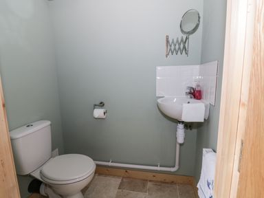 A small bathroom with a toilet, wall-mounted sink, mirror, and towel at The Stable at Church Farm House Limpenhoe near Reedham