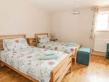 A bedroom with two single beds with floral bedding a small shelving unit and a turquoise ottoman at The Stable at Church Farm House Limpenhoe near Reedham