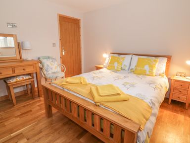 A bedroom with a wooden bed with yellow and white bedding and wooden furniture at The Stable at Church Farm House Limpenhoe near Reedham