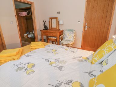 A bedroom with a bed covered with yellow and white bedding towels on the bed a wooden dressing table with a mirror a chair and wooden doors at The Stable at Church Farm House Limpenhoe near Reedham