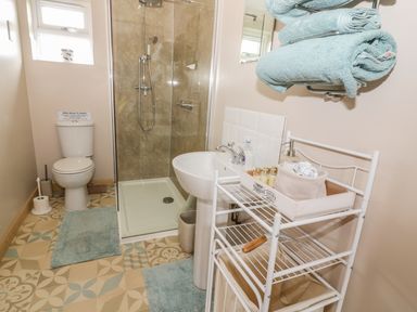 A bathroom with a toilet shower sink towel rack and storage shelves at The Stable at Church Farm House in Limpenhoe near Reedham