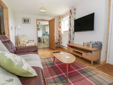 A living room with a brown leather sofa a wooden coffee table a wall-mounted television and a wooden TV stand at The Stable at Church Farm House Limpenhoe near Reedham