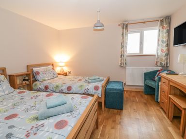 A bedroom with two single beds a wooden desk a teal chair and a window with patterned curtains at The Stable at Church Farm House Limpenhoe near Reedham