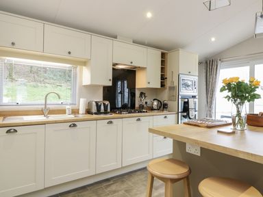 A kitchen with white cabinets a wooden countertop a stainless steel sink and two stools at Woodstock Lodge in Wemyss Bay