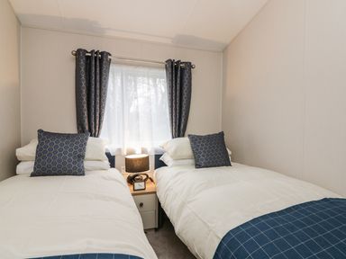 A bedroom with two single beds a nightstand a lamp and a window with curtains at Woodstock Lodge in Wemyss Bay