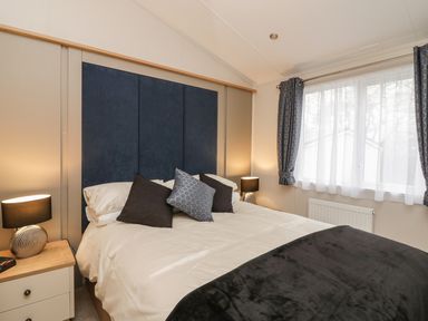 A bedroom with a bed with pillows and bedside tables with lamps and a window with curtains at Woodstock Lodge in Wemyss Bay