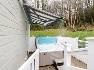 An outdoor hot tub with steps under a retractable awning next to a white fenced area and grass at Woodstock Lodge in Wemyss Bay