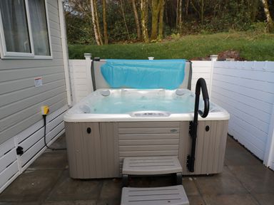 An outdoor hot tub with steps and a handrail next to a building and white fencing at Woodstock Lodge in Wemyss Bay