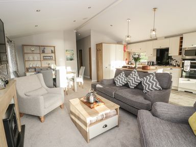 A living room with sofas and a coffee table next to a dining area and kitchen at Woodstock Lodge in Wemyss Bay