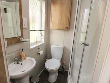 A bathroom with a sink mirror toilet wooden cabinet and shower cabin at Woodstock Lodge in Wemyss Bay