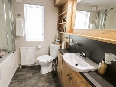 A bathroom with a toilet sink bathtub and wooden shelves at Woodstock Lodge in Wemyss Bay