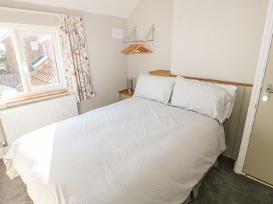 A bedroom with a double bed a window with floral curtains and a wall-mounted rack with hangers at 27 Whitegates Ludham
