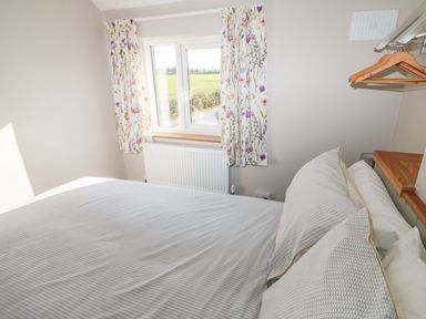 A bedroom with a bed near a window with floral curtains and wooden hangers at 27 Whitegates in Ludham