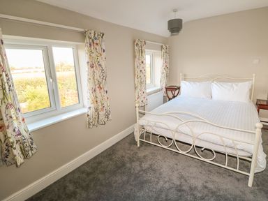 A bedroom with a metal frame bed white bedding floral curtains and two windows at 27 Whitegates in Ludham