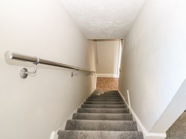A narrow staircase with grey carpet and a metal handrail at 27 Whitegates in Ludham