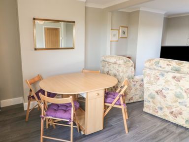 A dining area with a wooden table and folding chairs with purple cushions next to floral armchairs at 27 Whitegates in Ludham