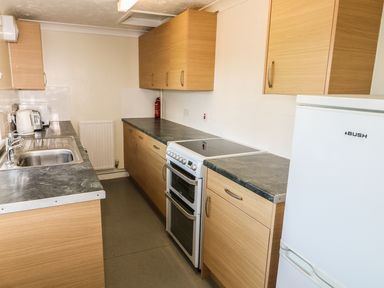 A kitchen with wooden cabinets black countertops a white electric stove a white fridge a stainless steel sink a kettle toaster and a fire extinguisher at 27 Whitegates Ludham