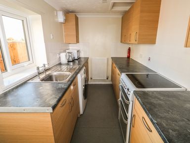 A kitchen with wooden cabinets a sink stove washing machine toaster kettle and microwave at 27 Whitegates in Ludham