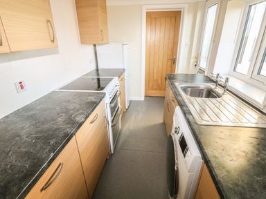 A kitchen with wooden cabinets a stove a washing machine and a sink at 27 Whitegates in Ludham