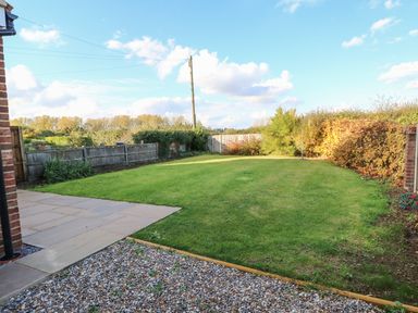 A backyard with a grass lawn a stone patio and a gravel area at 27 Whitegates in Ludham