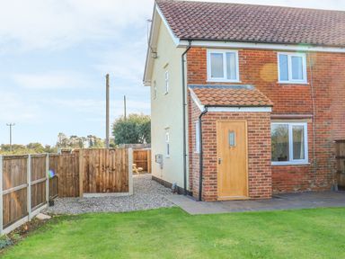 A backyard with grass a wooden fence and a brick house with a wooden door at 27 Whitegates in Ludham