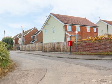 A street with houses fenced in wood and brick with a red mailbox on a pole at 27 Whitegates in Ludham