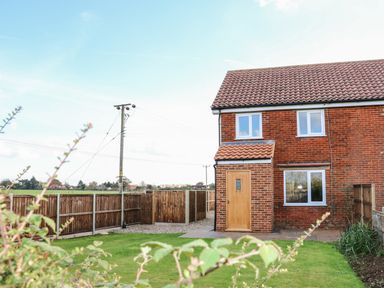 A brick house with a wooden door and windows next to a fenced yard and green lawn at 27 Whitegates in Ludham