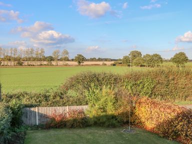 A garden with grass and shrubs overlooking farmland and trees at 27 Whitegates in Ludham