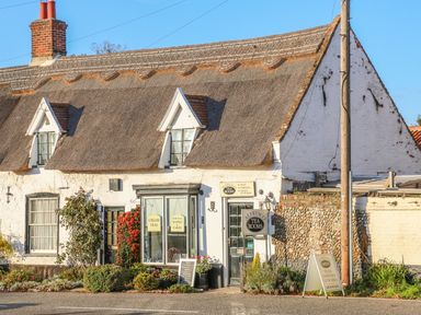 A thatched roof building with signs for Alfresco Tea Rooms and plants outside at 27 Whitegates in Ludham