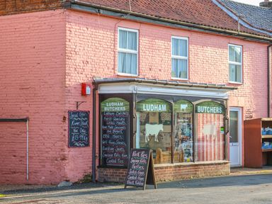 The exterior of a butcher shop with signs displaying meat products and prices at 27 Whitegates in Ludham